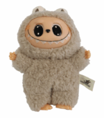 Primer plano de una figura coleccionable Labubu, un monstruo beige cubierto de peluche, con la cara, manos y pies de vinilo color piel, sonriendo ampliamente y con grandes ojos negros. Se aprecia la etiqueta de 'The Monsters' en el lateral.