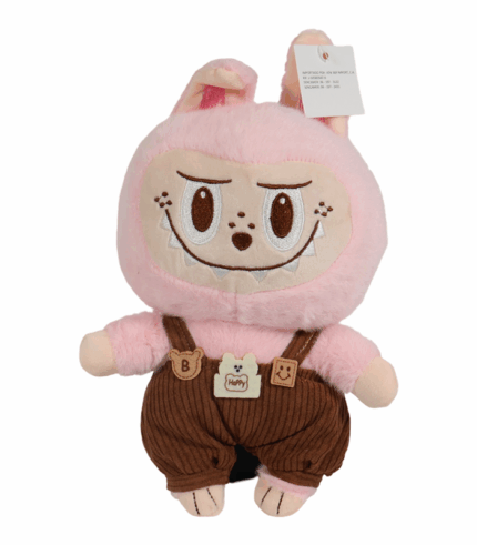 Peluche de personaje Labubu de color rosa pálido y textura suave. Viste unos overoles de pana marrón oscuro con tirantes y pequeños parches decorativos en forma de osos y una etiqueta que dice 'HAPPY'. El muñeco tiene orejas de conejo y una expresión sonriente y pícara con dientes bordados.